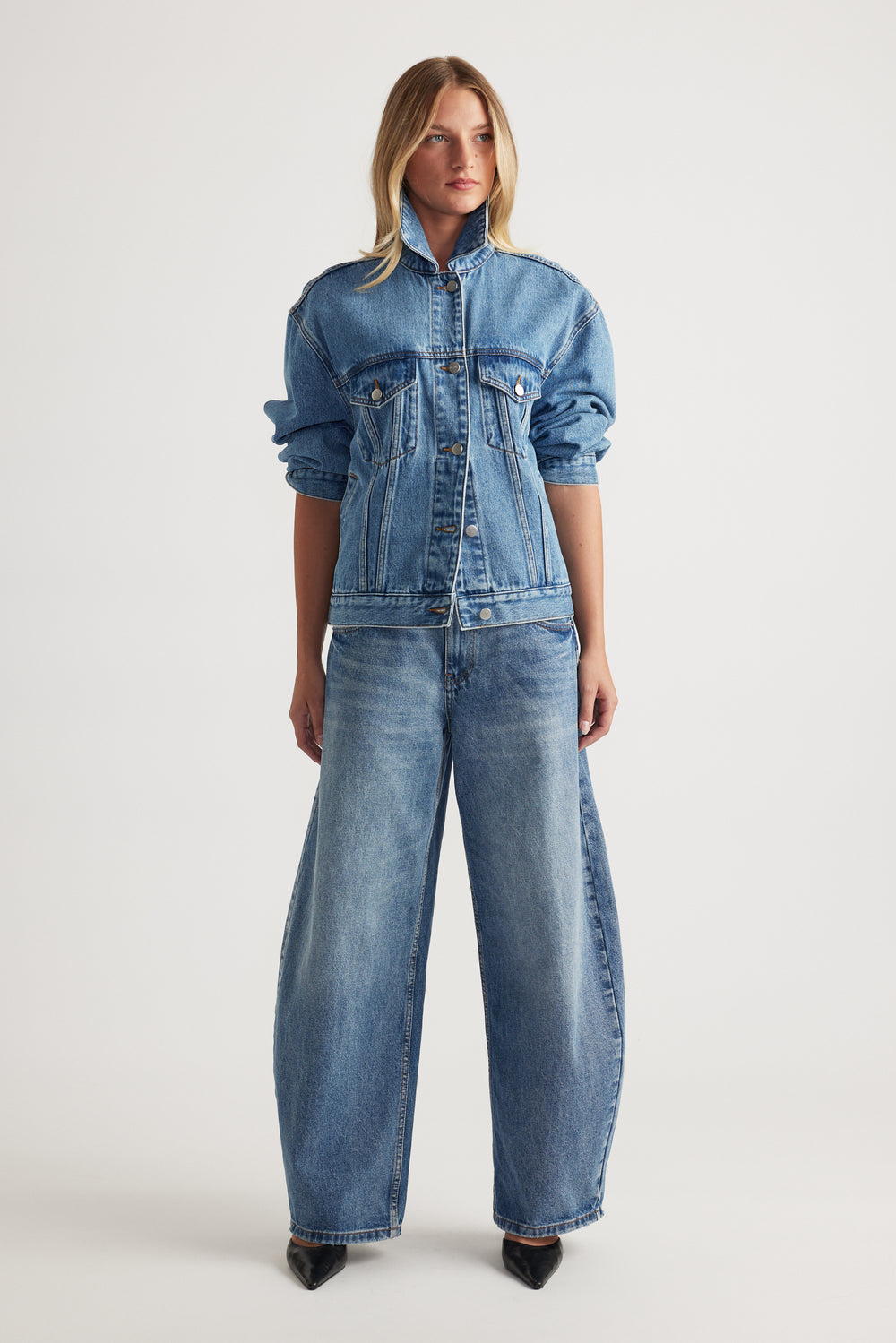 Model wearing full length high rise horseshoe jeans with a curved wide leg and matching denim jacket