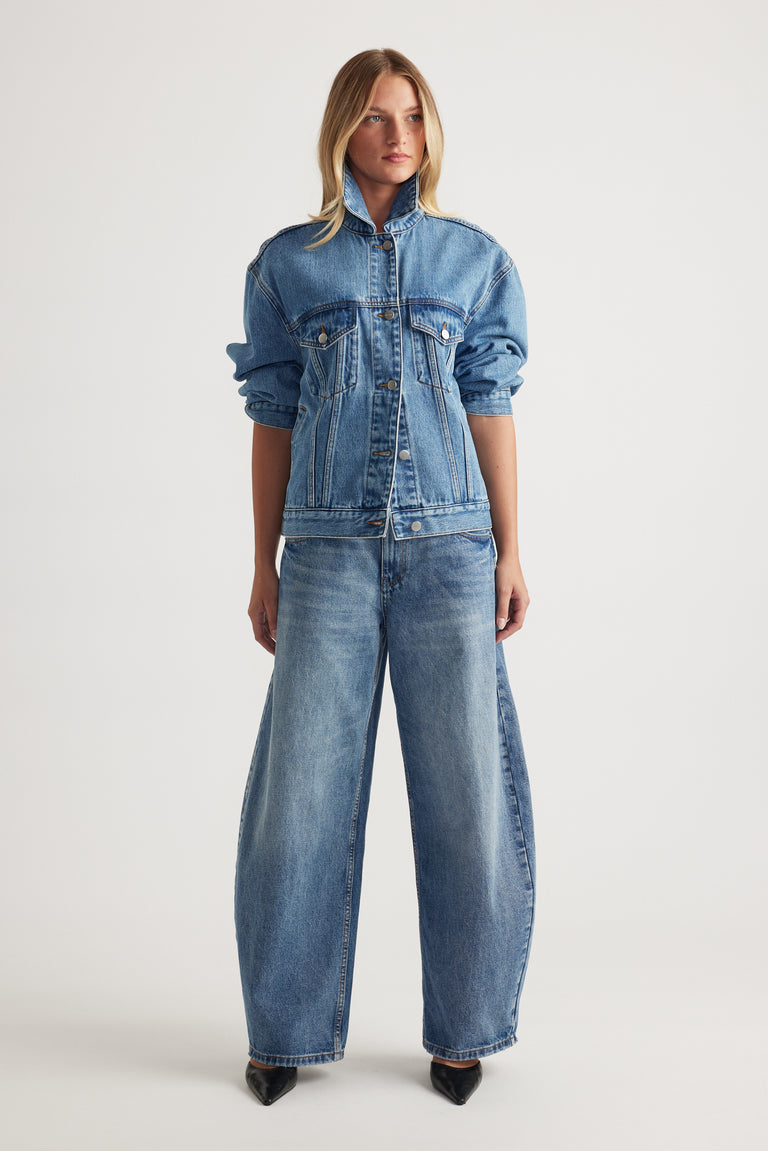 Model wearing full length high rise horseshoe jeans with a curved wide leg and matching denim jacket