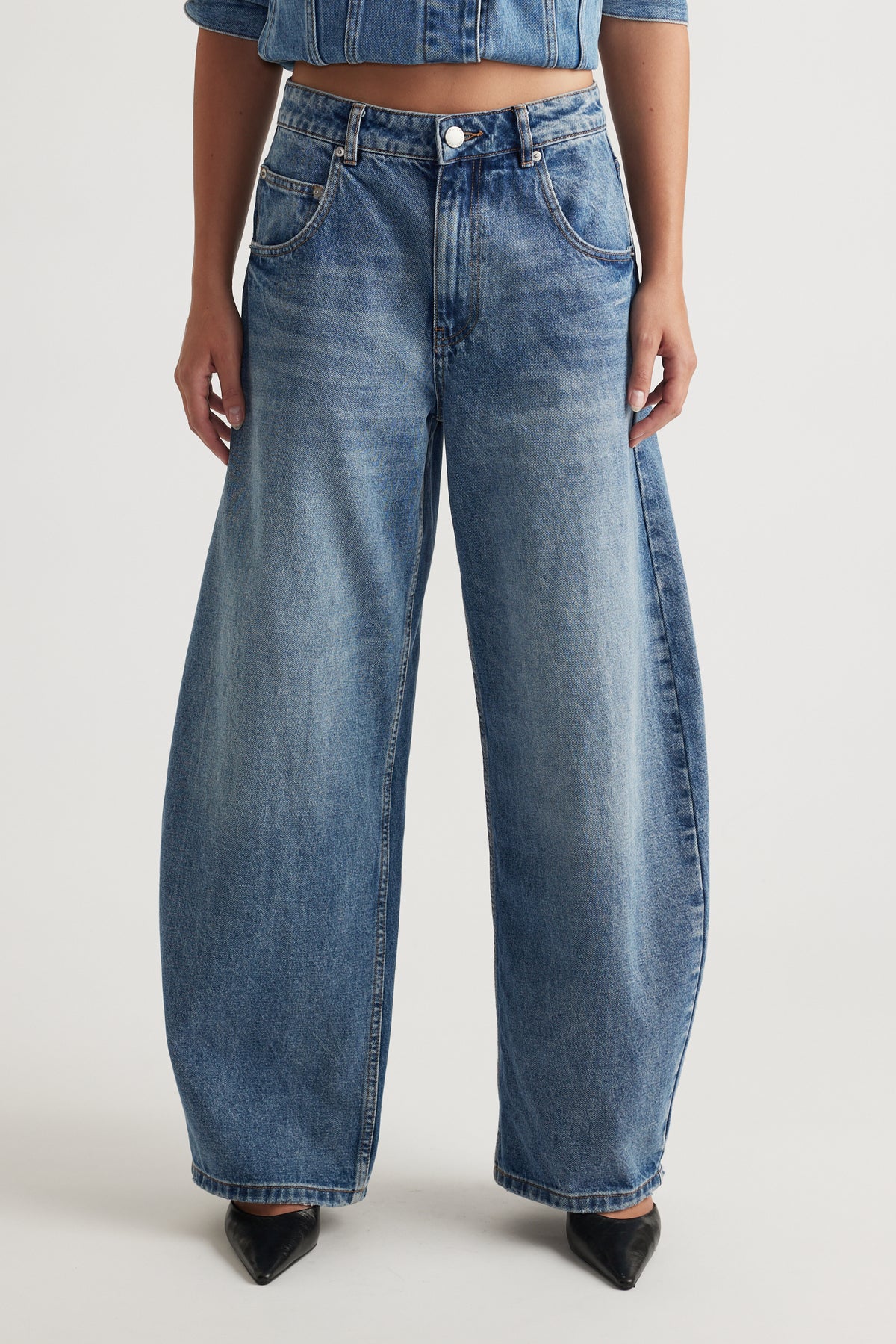 Woman wearing high rise blue horseshoe jeans with a curved wide leg and tapered ankle