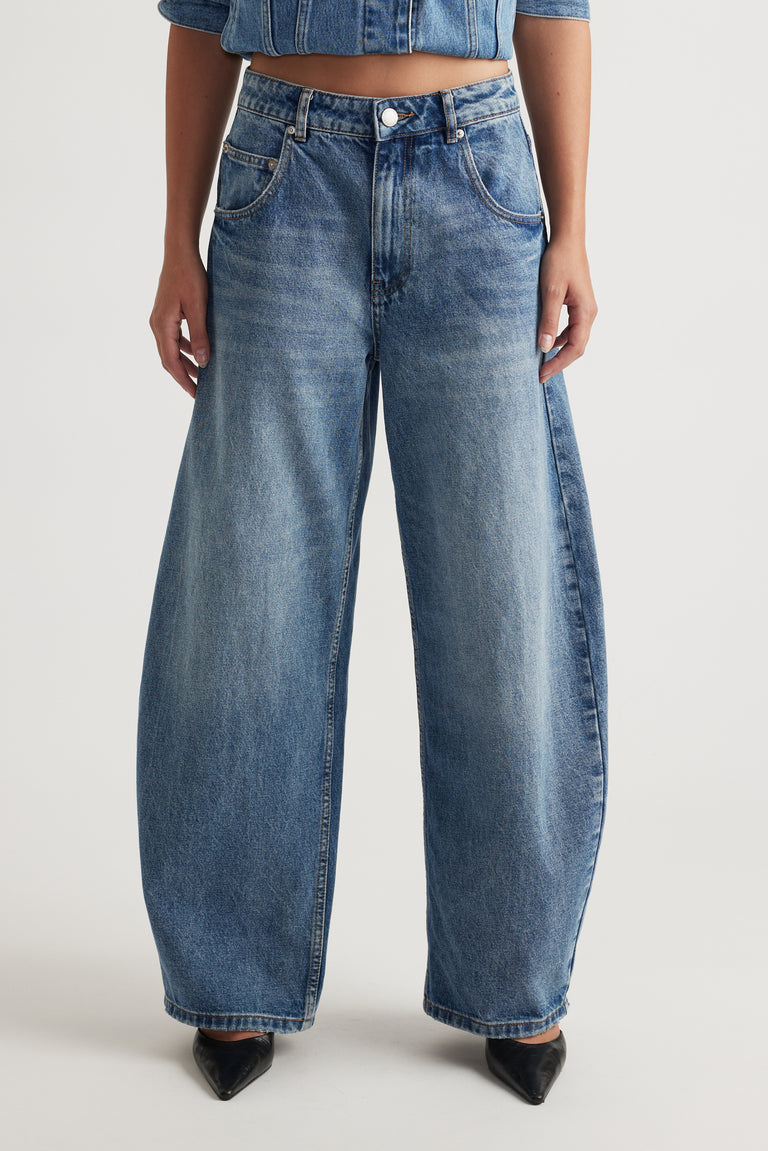 Woman wearing high rise blue horseshoe jeans with a curved wide leg and tapered ankle