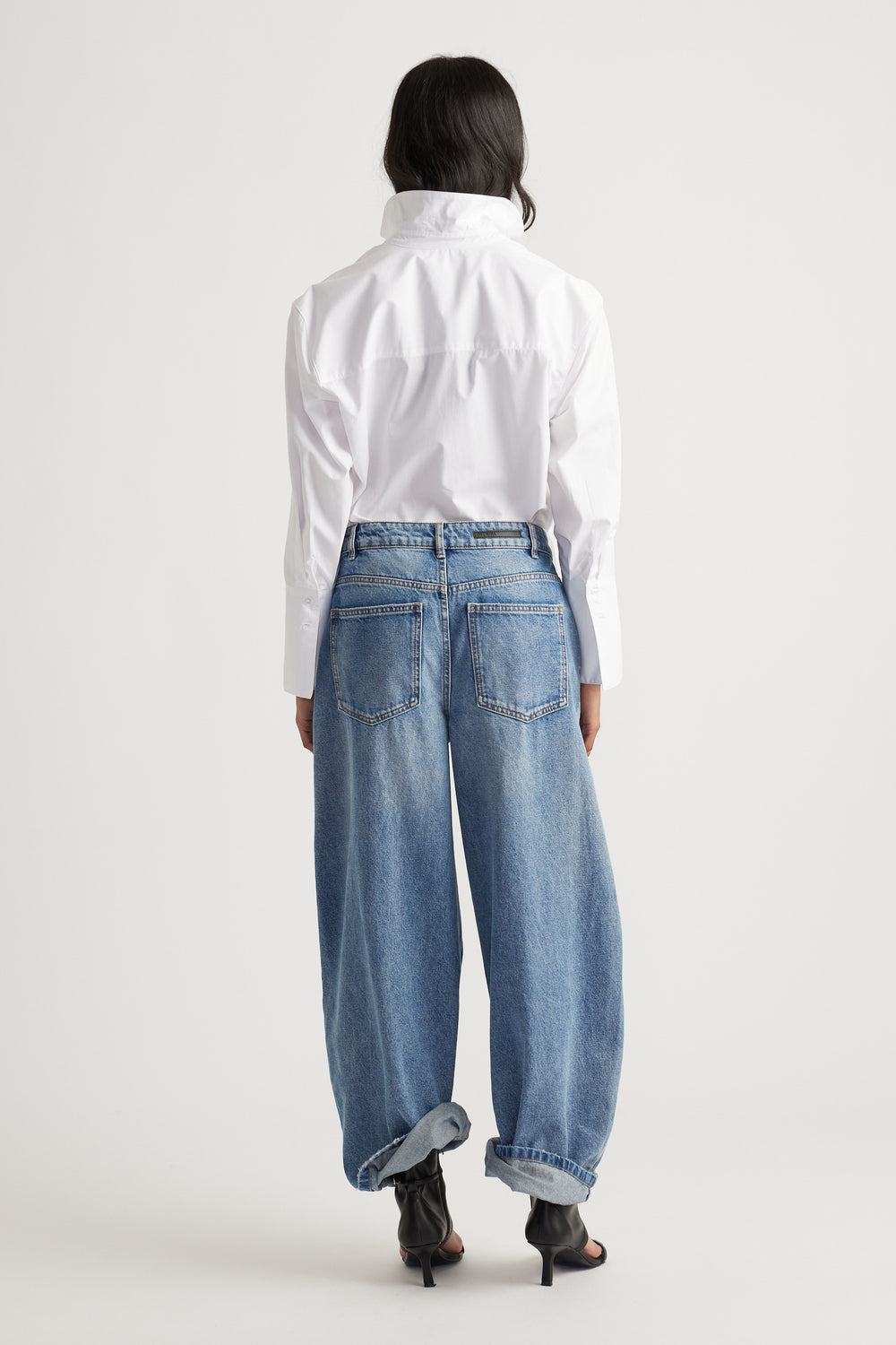 Woman wearing blue high rise horseshoe jeans with curved wide legs and a white button up shirt