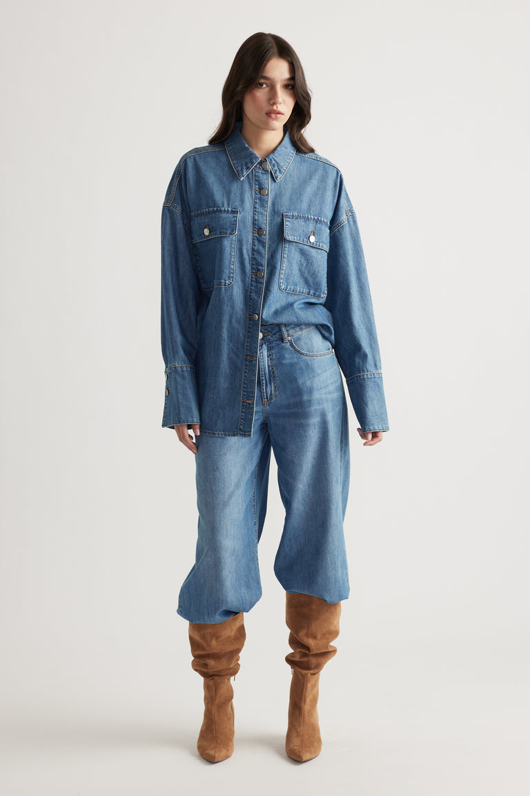 Model wearing a relaxed-fit medium blue denim shirt with patch pockets, paired with loose denim pants and tan slouch boots