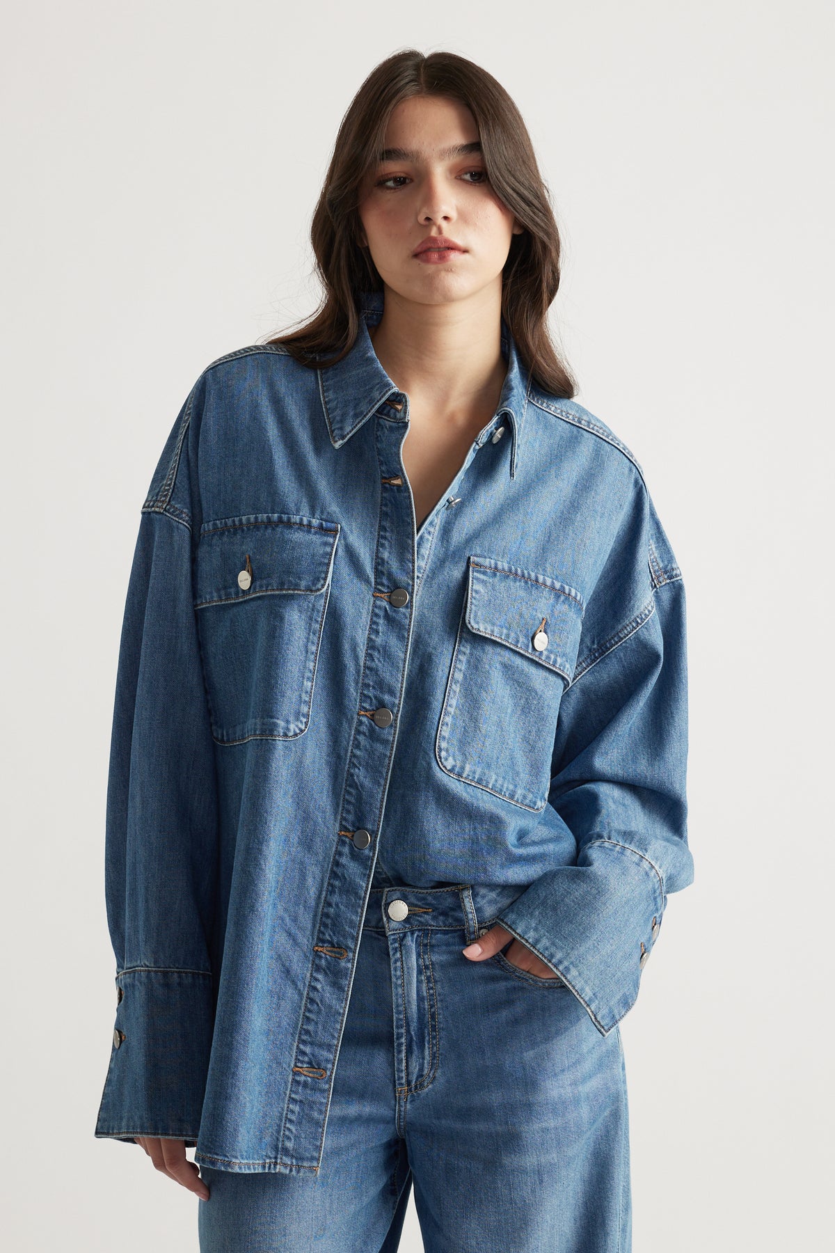 Woman wearing a relaxed fit medium blue denim shirt with large front pockets, paired with matching denim jeans