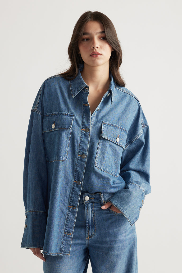Woman wearing a relaxed fit medium blue denim shirt with large front pockets, paired with matching denim jeans