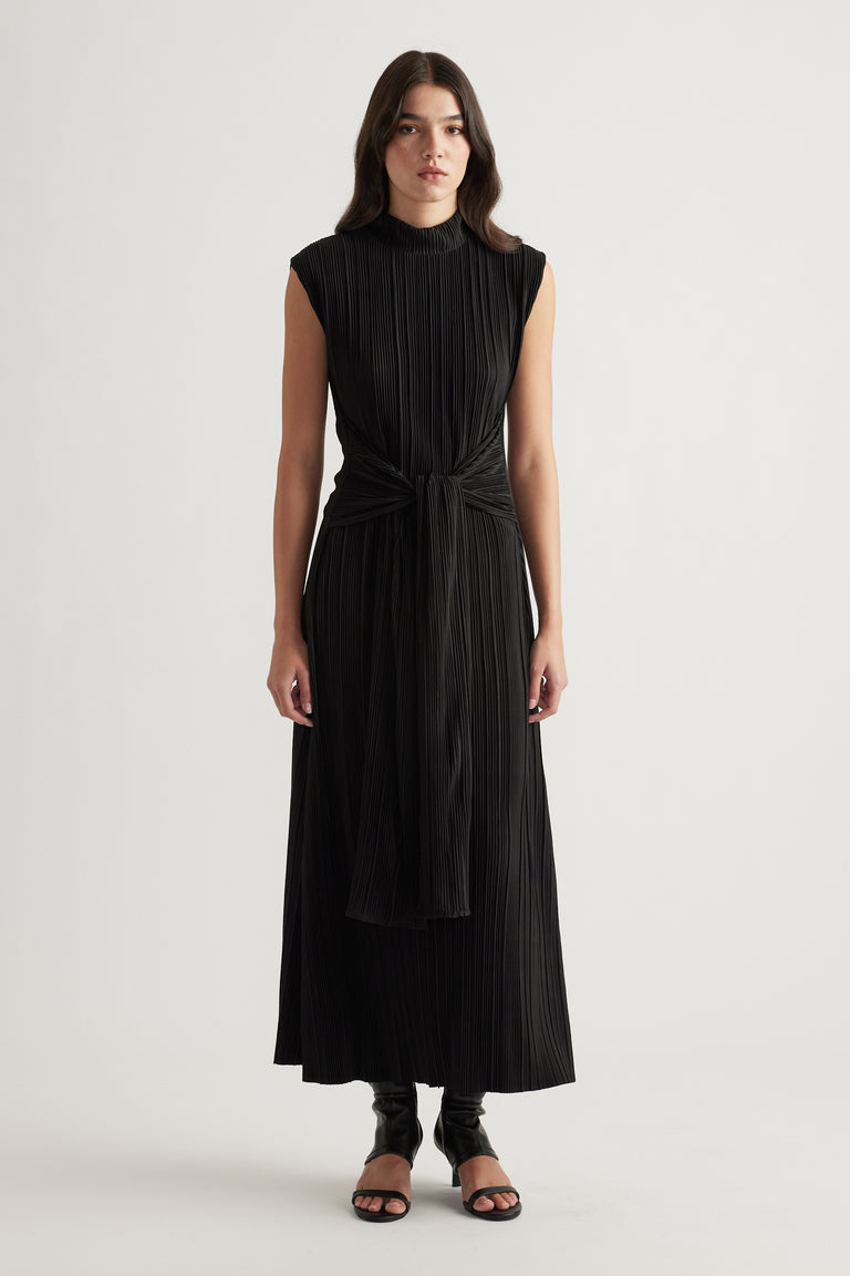Sleeveless black maxi dress with pleated texture and front tie detail, styled with open-toe heels for a sleek look