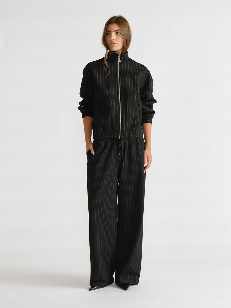 Woman wearing a black D-Luxe Pinstripe Bomber with subtle pinstripes, zip front, and matching wide-leg pants for modern layering.