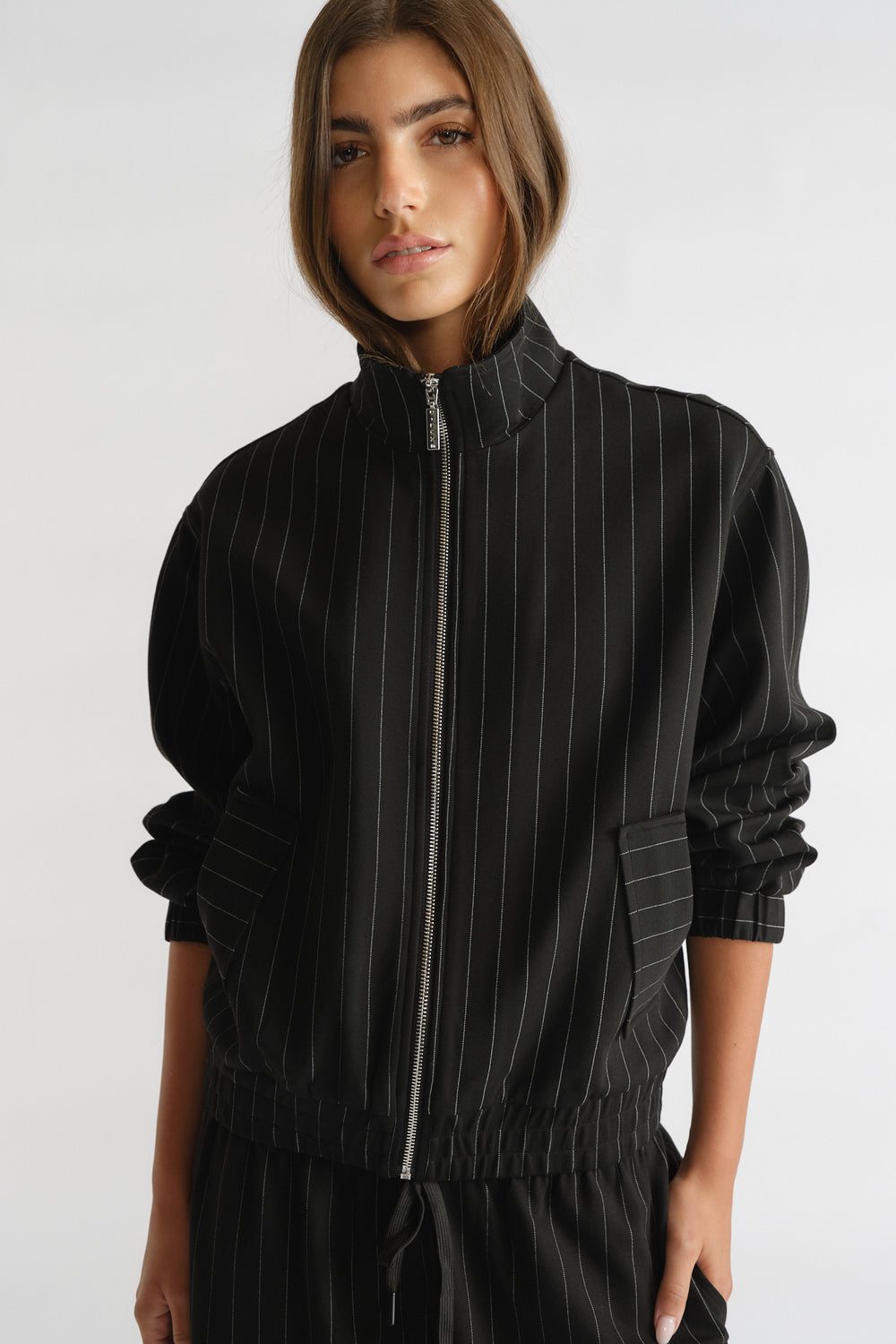 Woman wearing black D-Luxe Pinstripe Bomber with subtle vertical stripes, zip front, and relaxed fit for everyday versatile style.