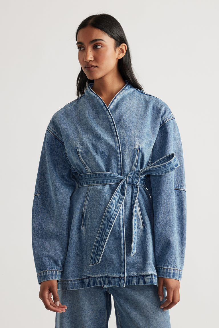 Woman wearing Kylie Denim Blazer Dress in light blue wash, featuring wrap front and self-tie belt with relaxed fit.