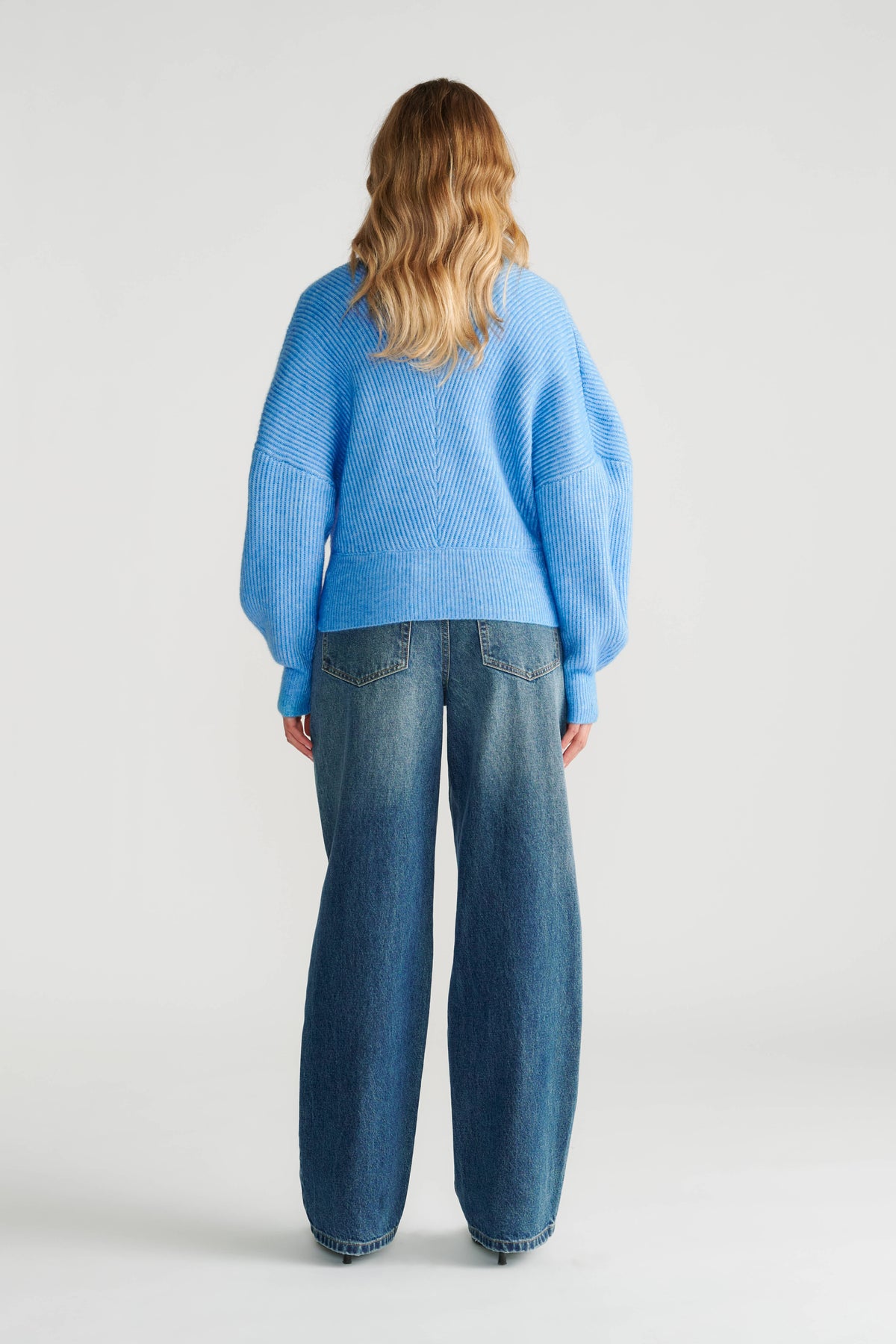 Woman wearing a relaxed fit azure blue knit jumper paired with loose straight-leg denim jeans, back view.