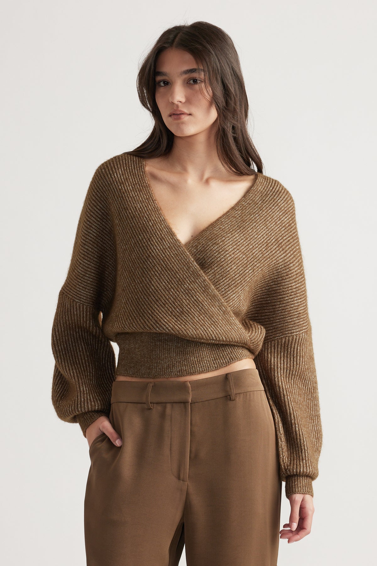 Woman wearing a bronze ribbed crossover jumper with balloon sleeves paired with tailored brown high-waist pants