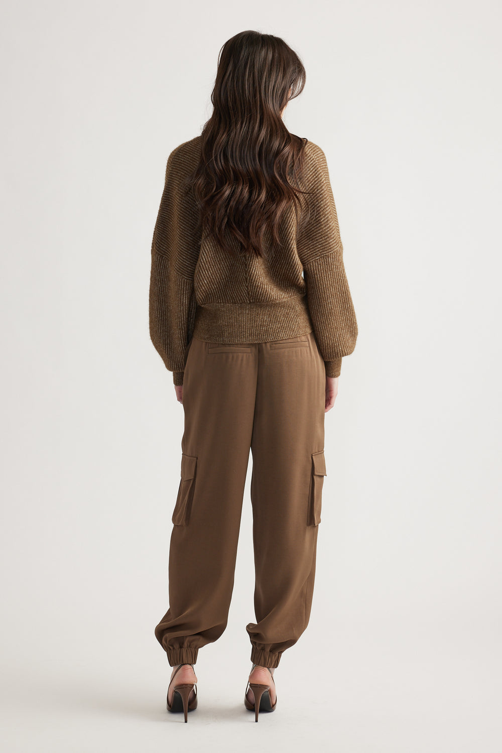 Woman with long wavy hair wearing a bronze knit jumper and relaxed-fit cargo pants with elastic cuffs and heels