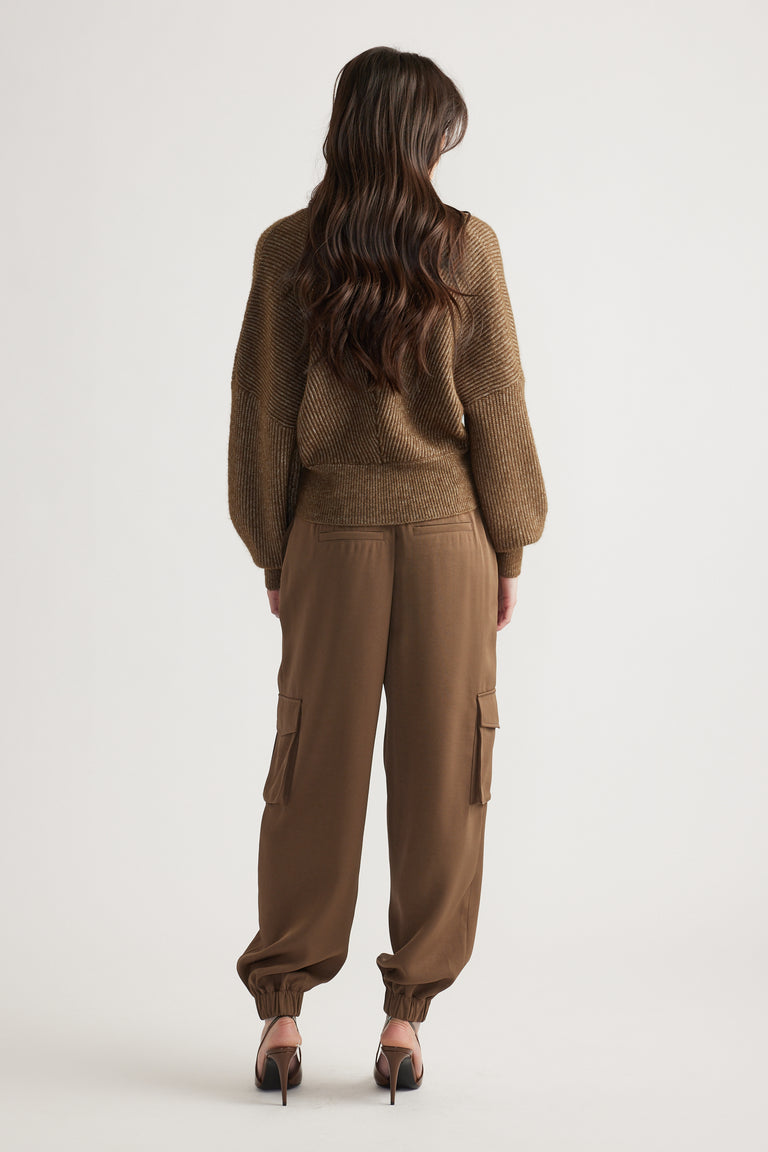 Woman with long wavy hair wearing a bronze knit jumper and relaxed-fit cargo pants with elastic cuffs and heels