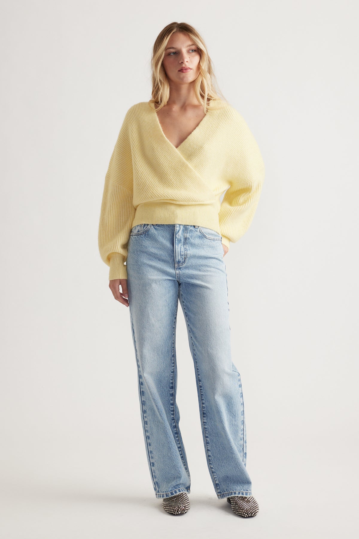 Woman wearing a soft lemon crossover jumper paired with light blue straight-leg jeans and patterned shoes