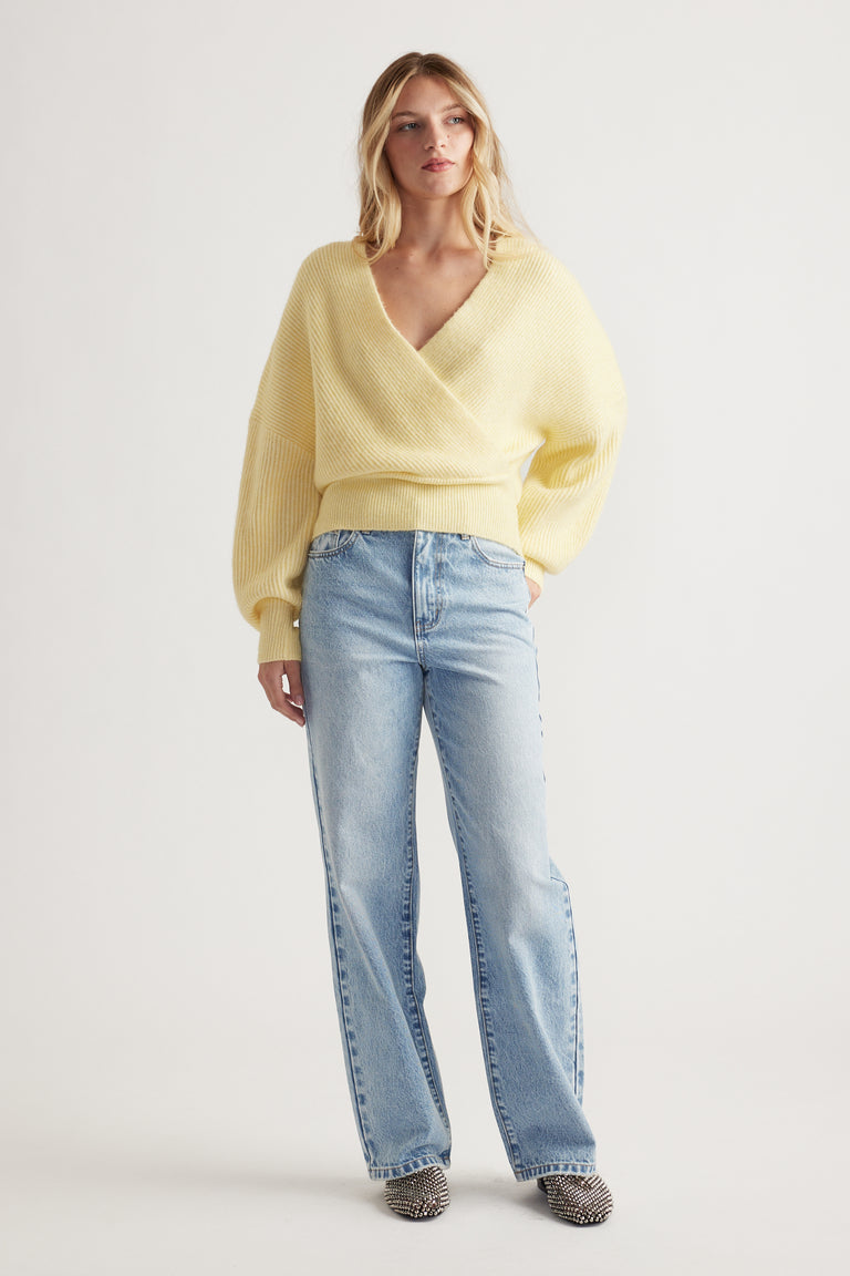 Woman wearing a soft lemon crossover jumper paired with light blue straight-leg jeans and patterned shoes