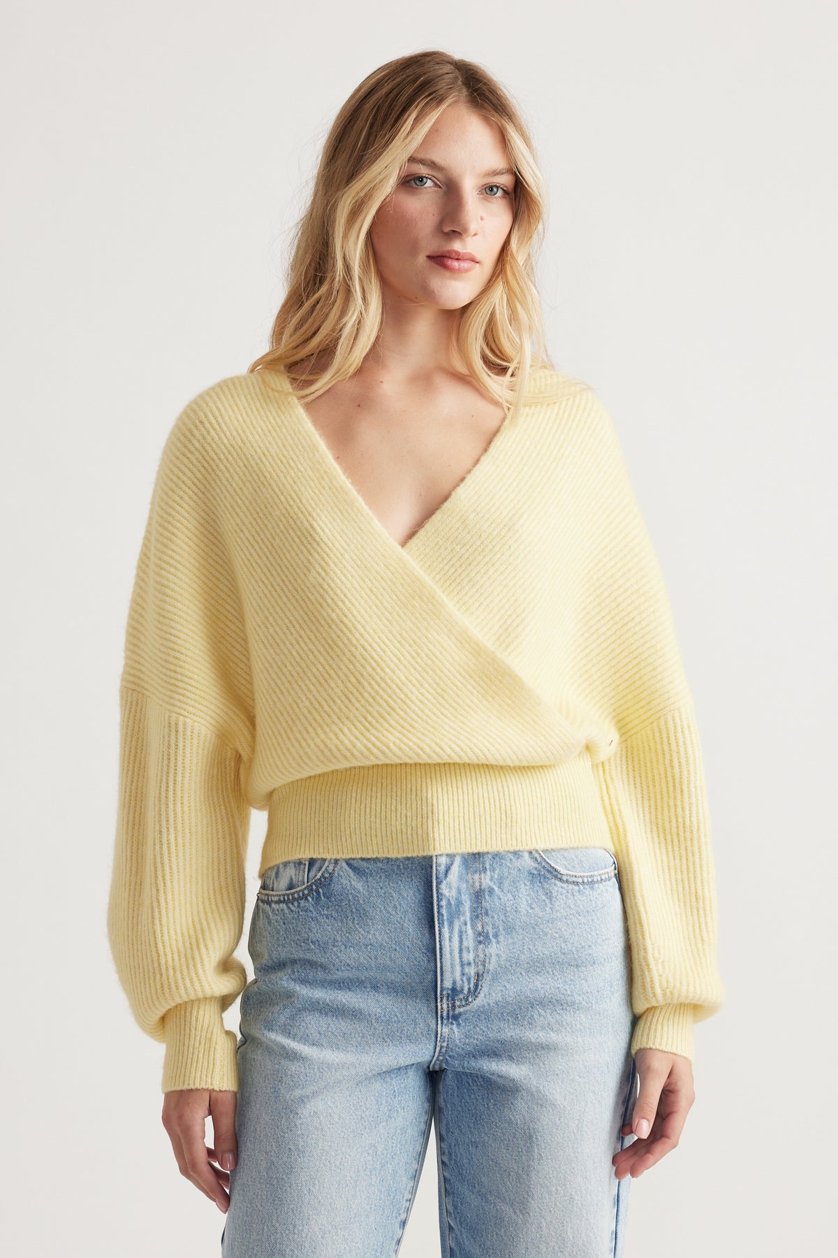 Woman wearing a soft yellow crossover jumper with balloon sleeves paired with light blue high-waisted jeans
