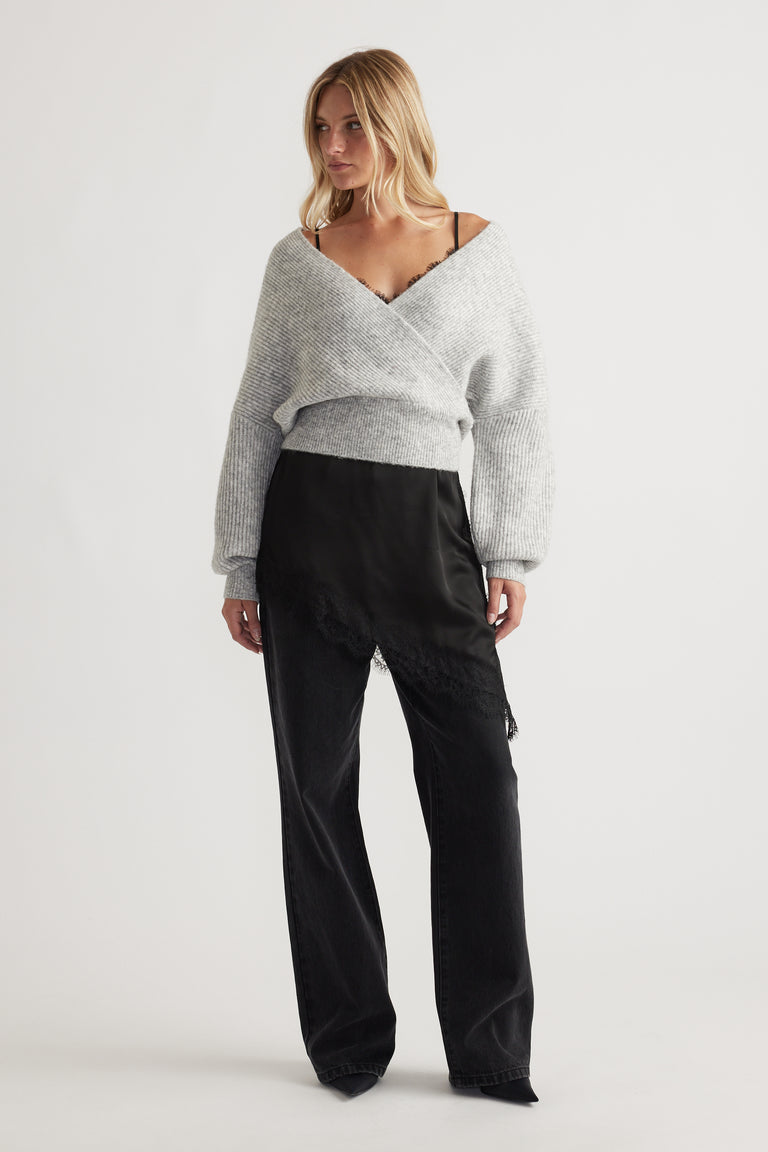 Woman wearing a light grey crossover knit jumper with voluminous sleeves paired with black satin wide-leg pants with lace trim