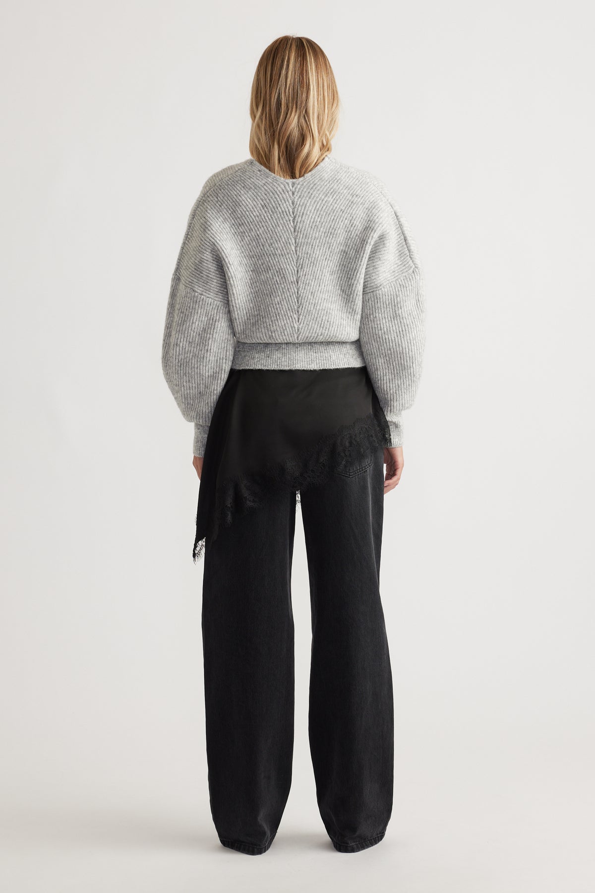 Woman seen from behind wearing a light grey knit jumper with balloon sleeves and wide-leg black pants with lace detail