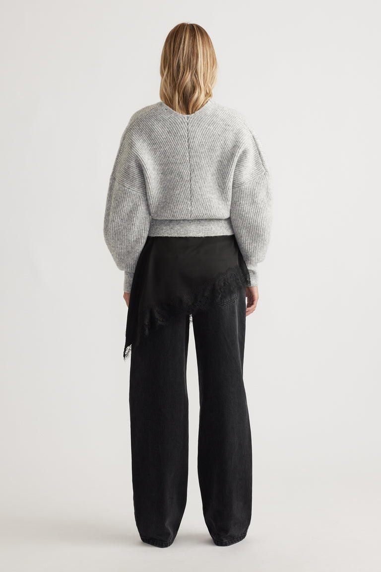 Woman seen from behind wearing a light grey knit jumper with balloon sleeves and wide-leg black pants with lace detail