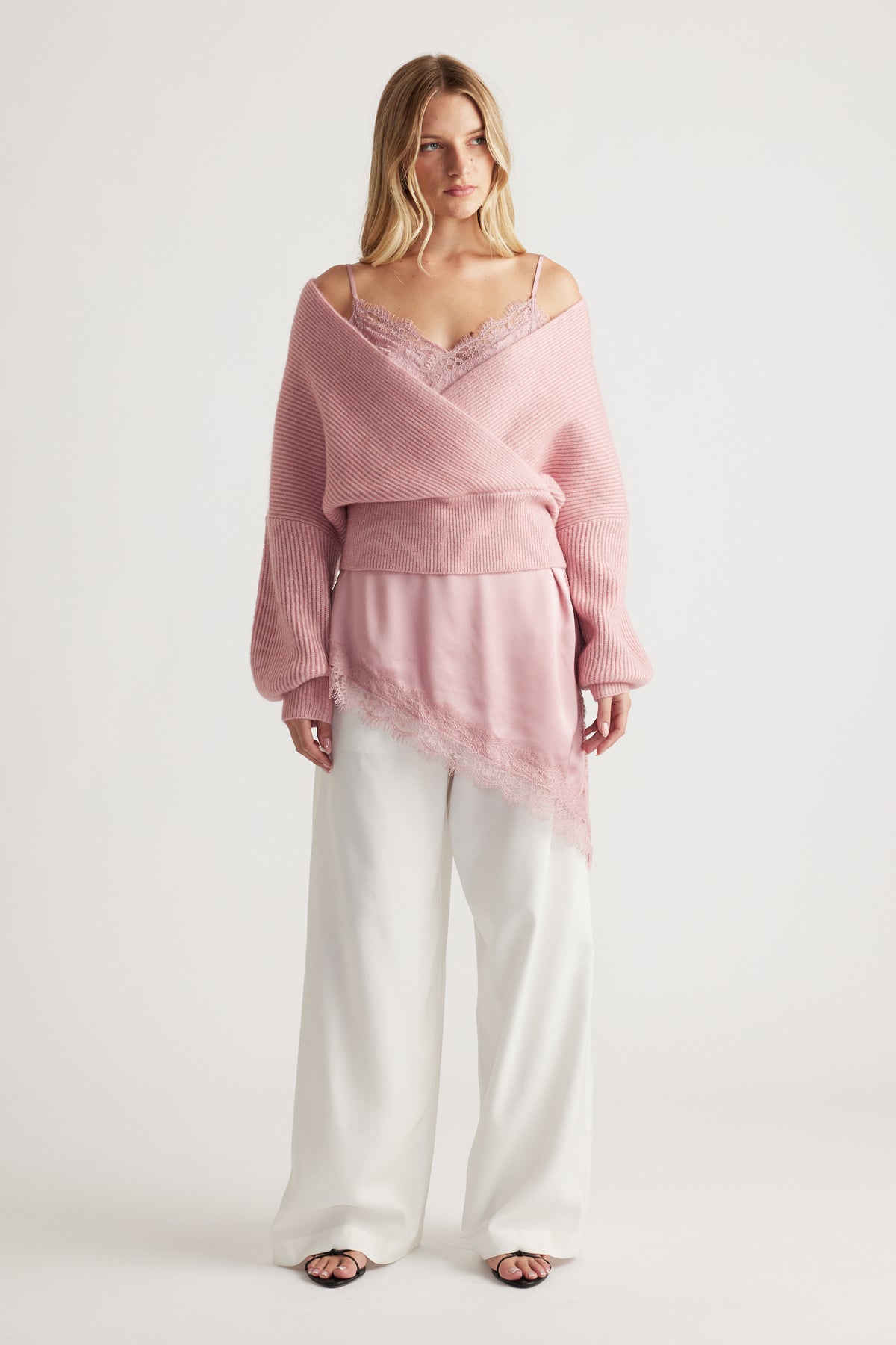 Soft pink crossover knit jumper layered over a lace-trimmed camisole, paired with relaxed white wide-leg pants.