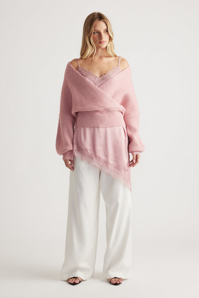 Soft pink crossover knit jumper layered over a lace-trimmed camisole, paired with relaxed white wide-leg pants.