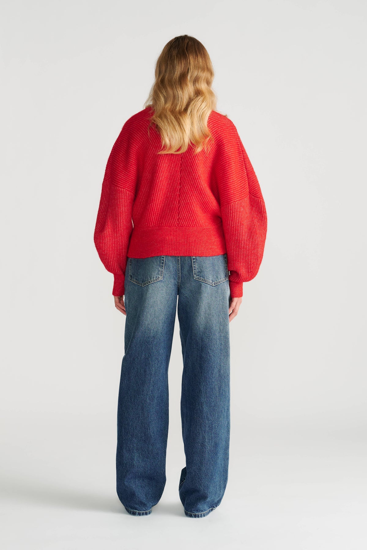 Woman seen from behind wearing a bright red oversized jumper with textured knit and relaxed wide-leg blue jeans.