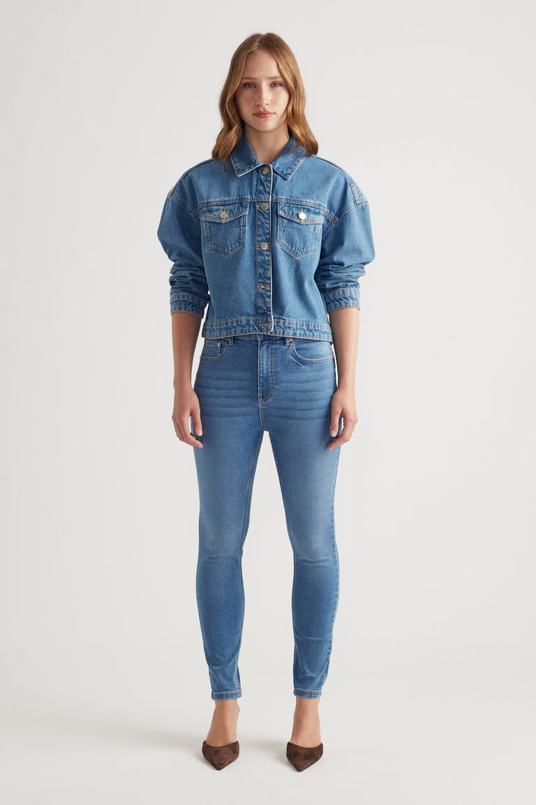 Woman wearing mid-blue denim jacket with chest pockets and slim blue jeans for a stylish casual denim look