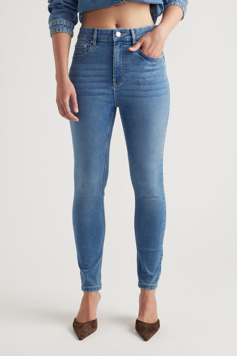 Slim fit mid-blue denim jeans with subtle whiskering details, styled with a cropped jacket and brown pointed shoes.