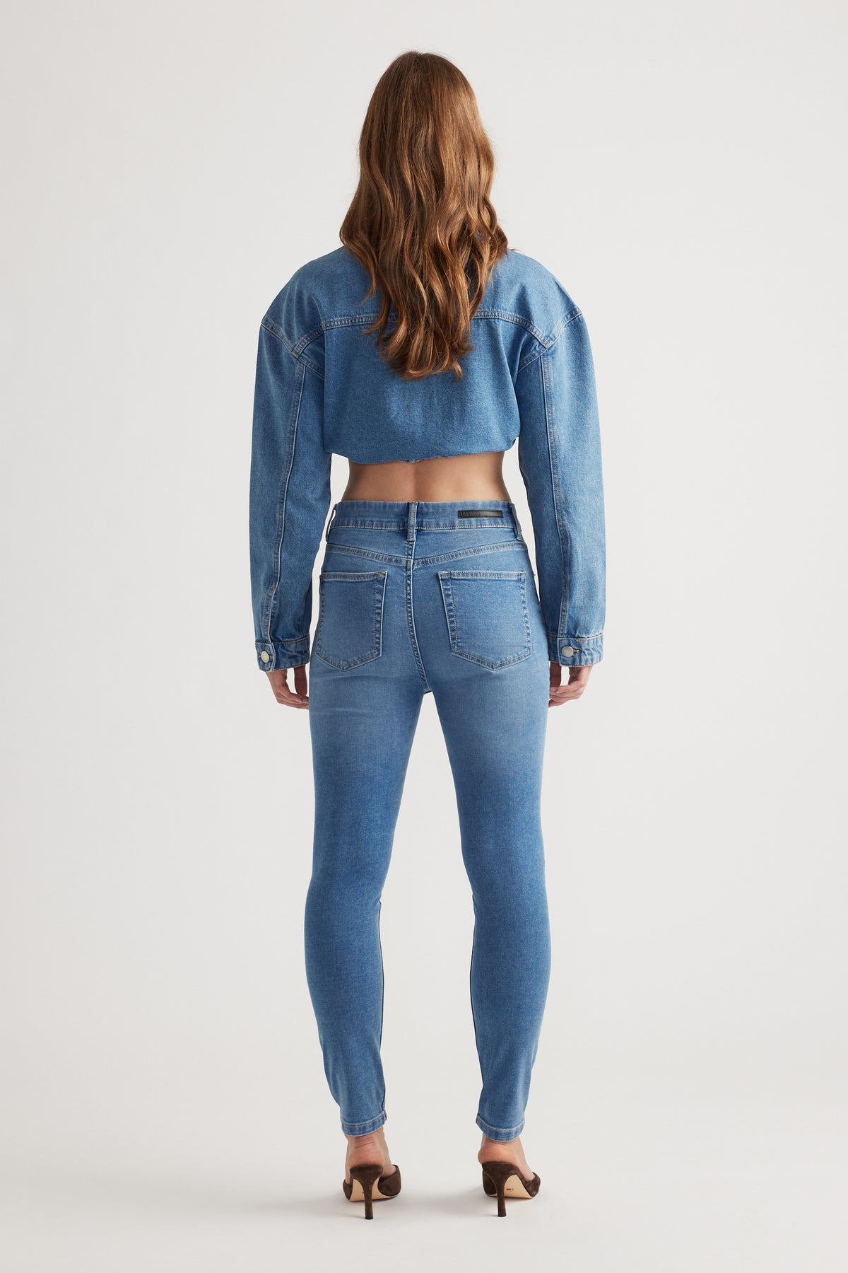 Woman wearing mid-blue skinny denim jeans paired with a cropped denim jacket and heels for a chic look