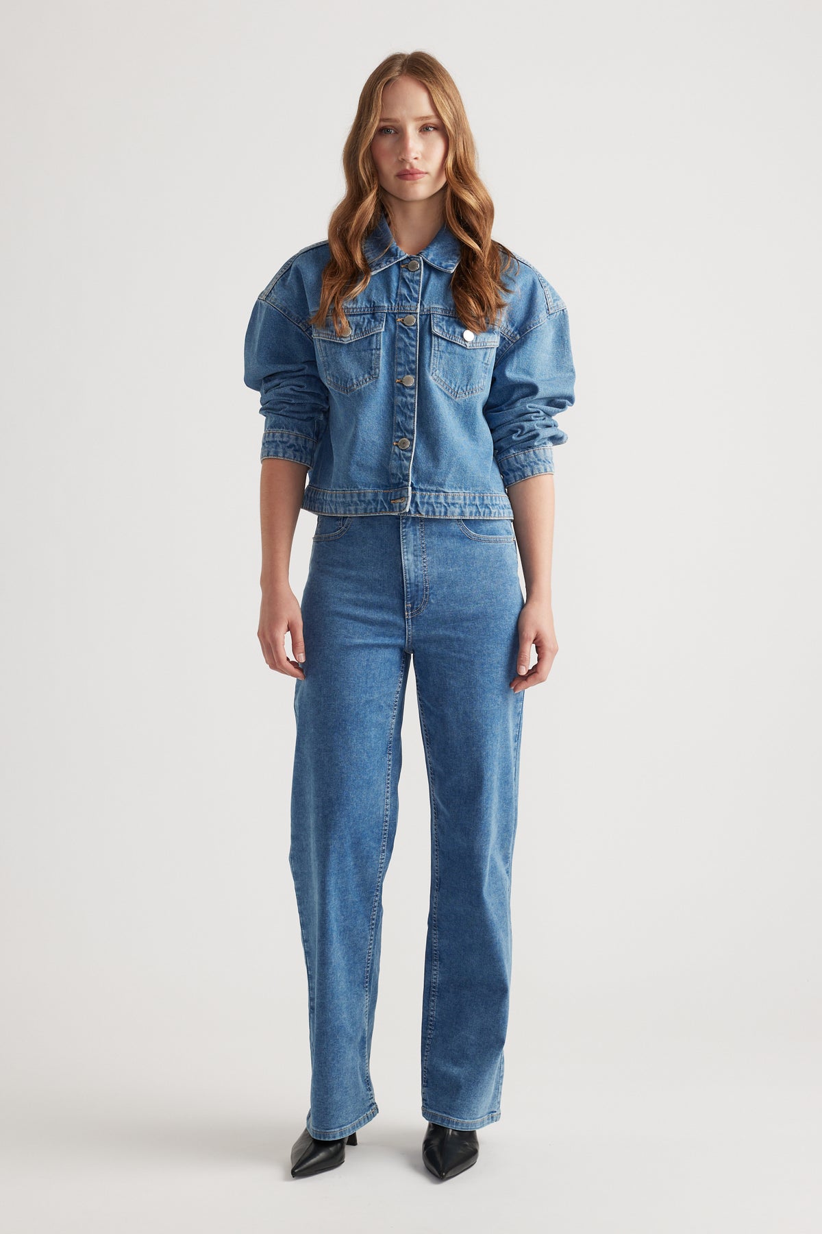 Woman wearing mid-blue denim jacket with voluminous sleeves paired with high-waisted straight leg jeans and black pointed shoes