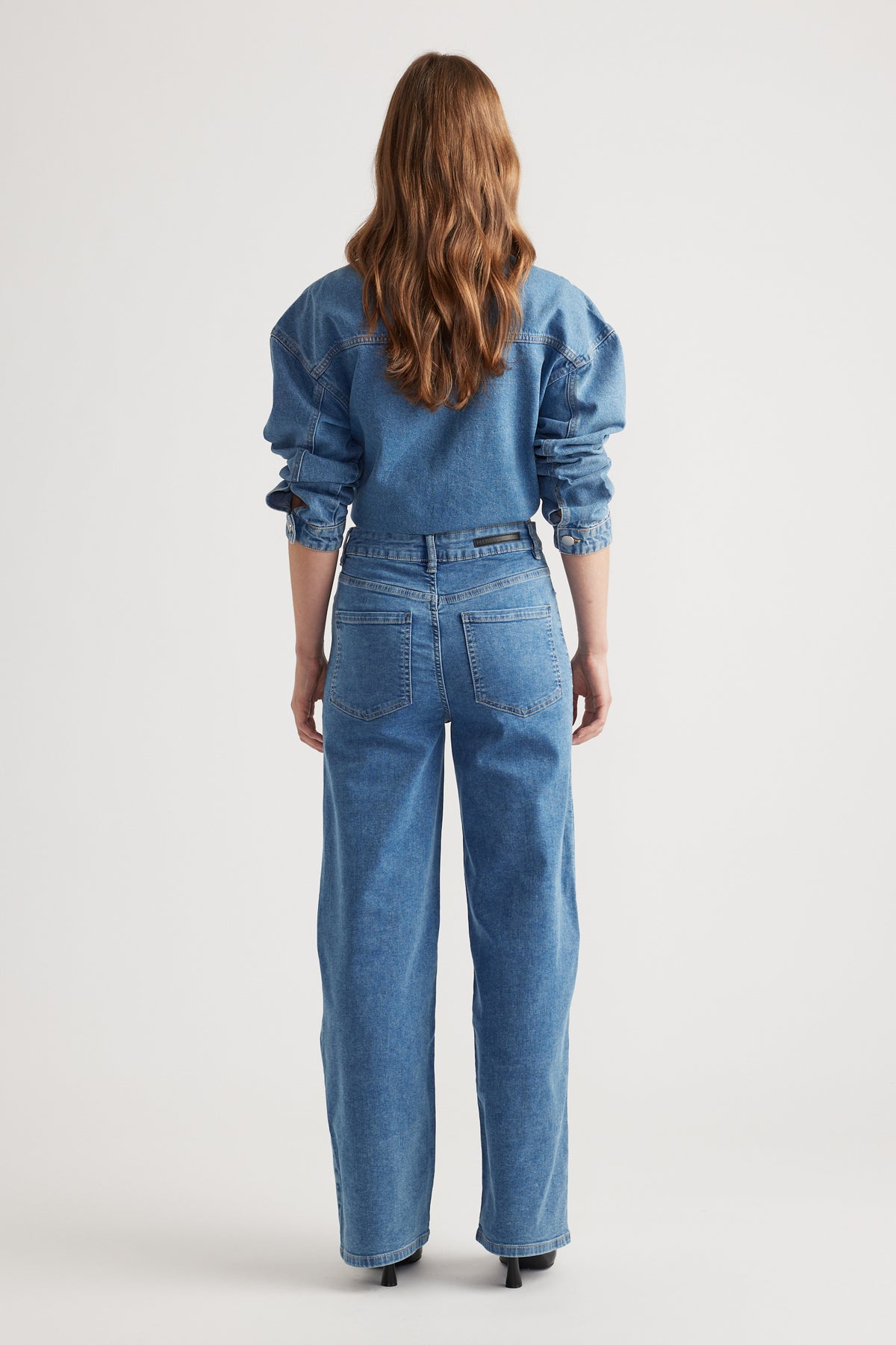 Woman wearing mid-blue straight-leg denim jeans styled with a matching denim jacket and black heels for a polished look