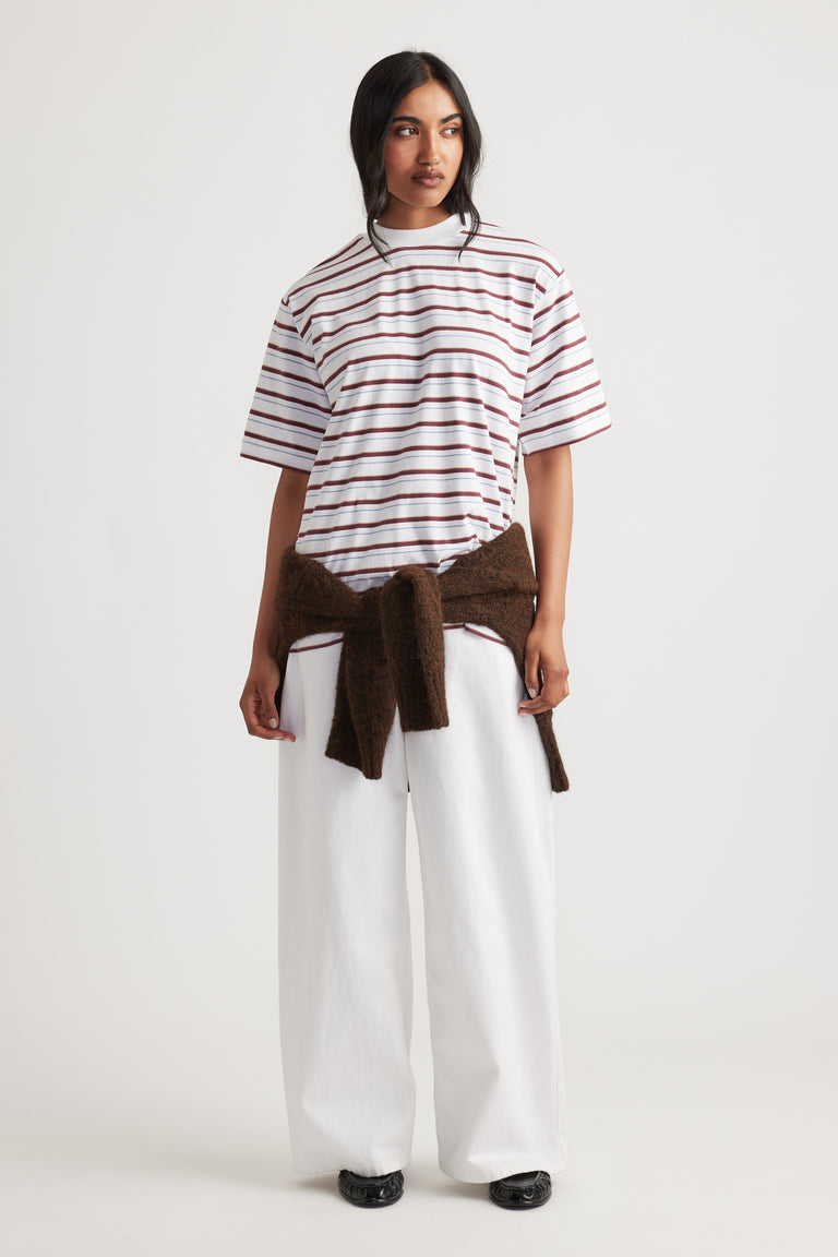 Woman wearing Isabella Oversized Stripe Tee in white with brown stripes, styled with wide-leg white pants and a brown sweater by DECJUBA