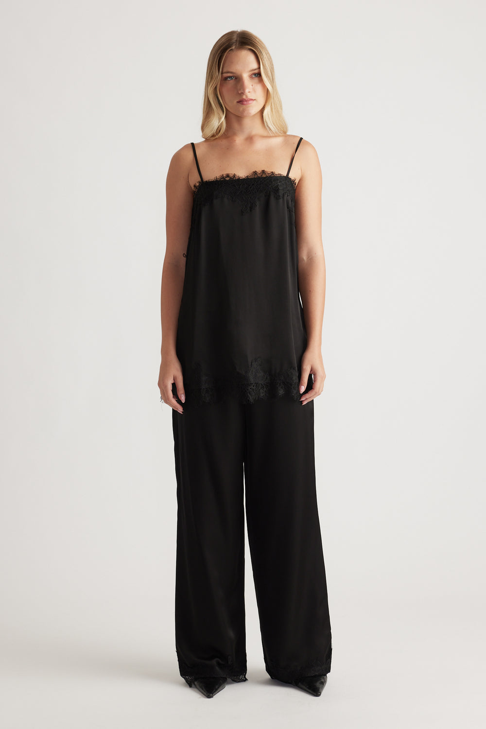 Woman wearing a loose black lace-trimmed camisole top with thin straps paired with wide-leg black pants