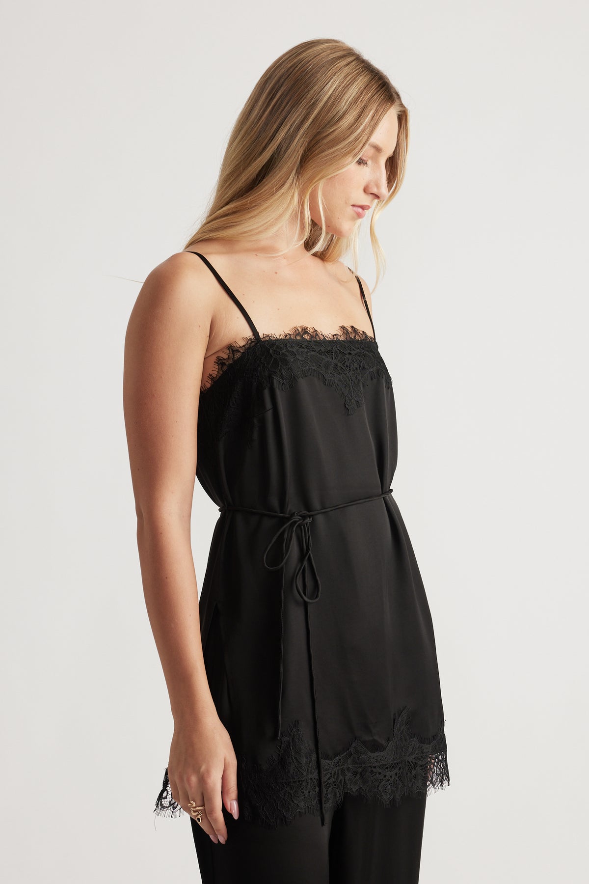 Side view of a woman wearing a black lace-trimmed camisole top with thin straps and a waist tie detail