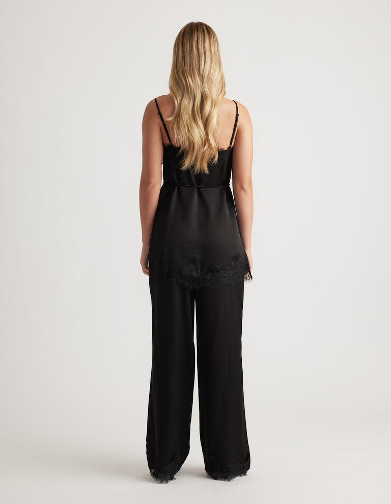 Back view of a woman wearing a black lace-trimmed camisole top with matching wide-leg pants and gold-toned strap details