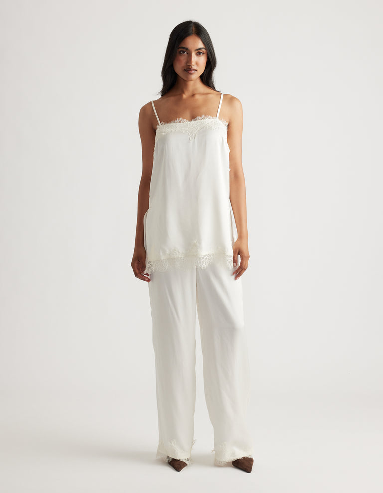 Woman wearing a delicate ivory lace-trimmed camisole top paired with loose matching wide-leg pants, styled simply.