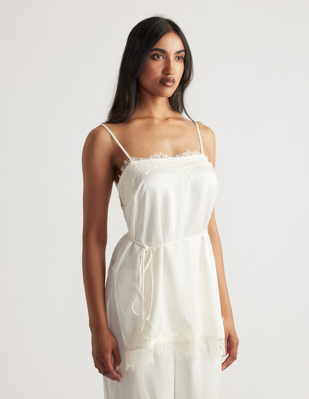 Woman wearing an ivory lace-trimmed camisole top with a square neckline and adjustable thin straps