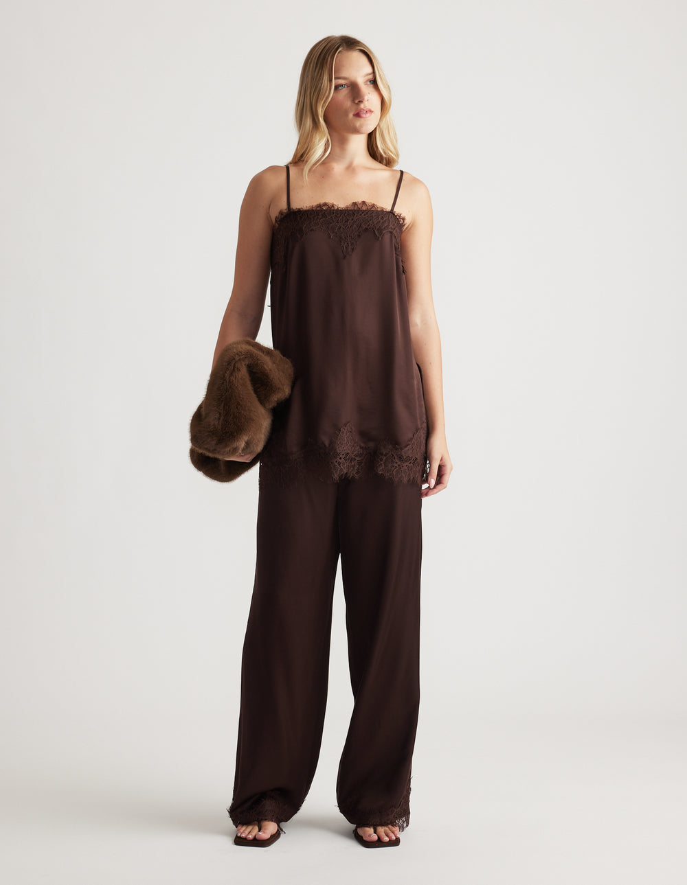 Woman wearing a rich mocha lace-trimmed cami top with matching wide-leg pants and holding a plush brown jacket