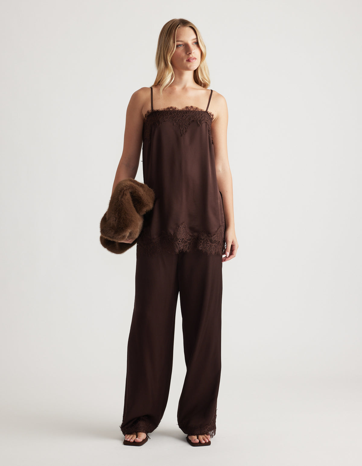 Woman wearing a rich mocha lace-trimmed cami top with matching wide-leg pants and holding a plush brown jacket