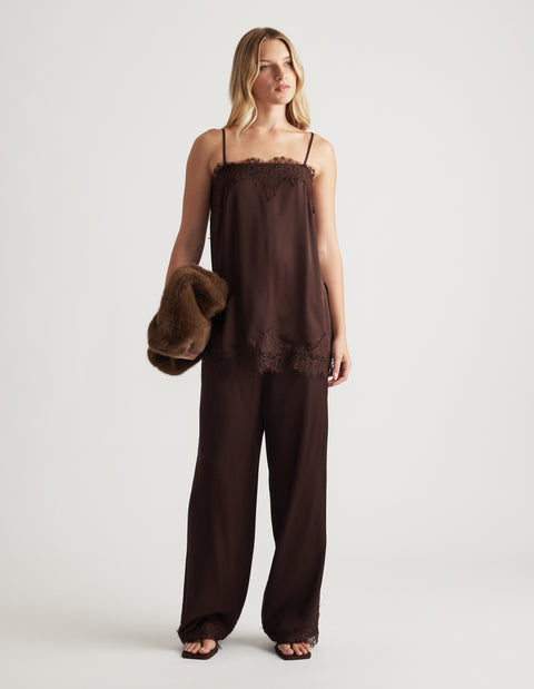 Woman wearing a rich mocha lace-trimmed cami top with matching wide-leg pants and holding a plush brown jacket