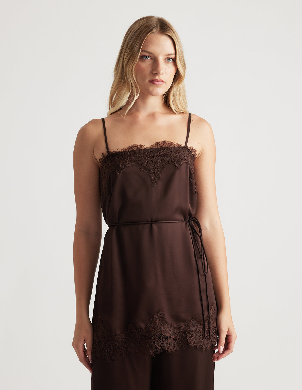 Woman wearing rich mocha lace-trimmed camisole top with delicate spaghetti straps and a slim waist tie for an elegant look.