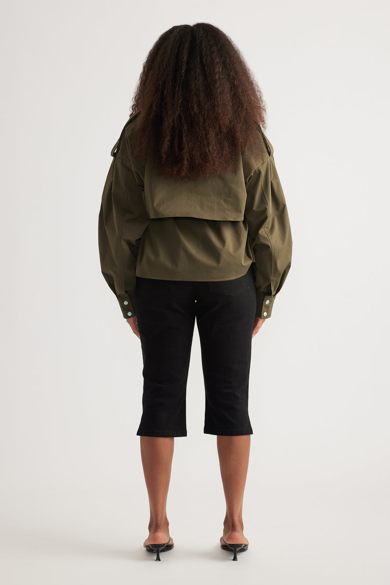 Back view of a woman in an olive cropped trench coat, black cropped pants and heeled sandals