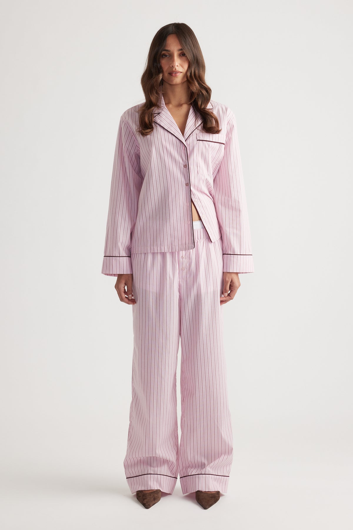 Woman wearing soft pink striped sleep wide leg pants and matching button-up long sleeve top with contrast piping trim