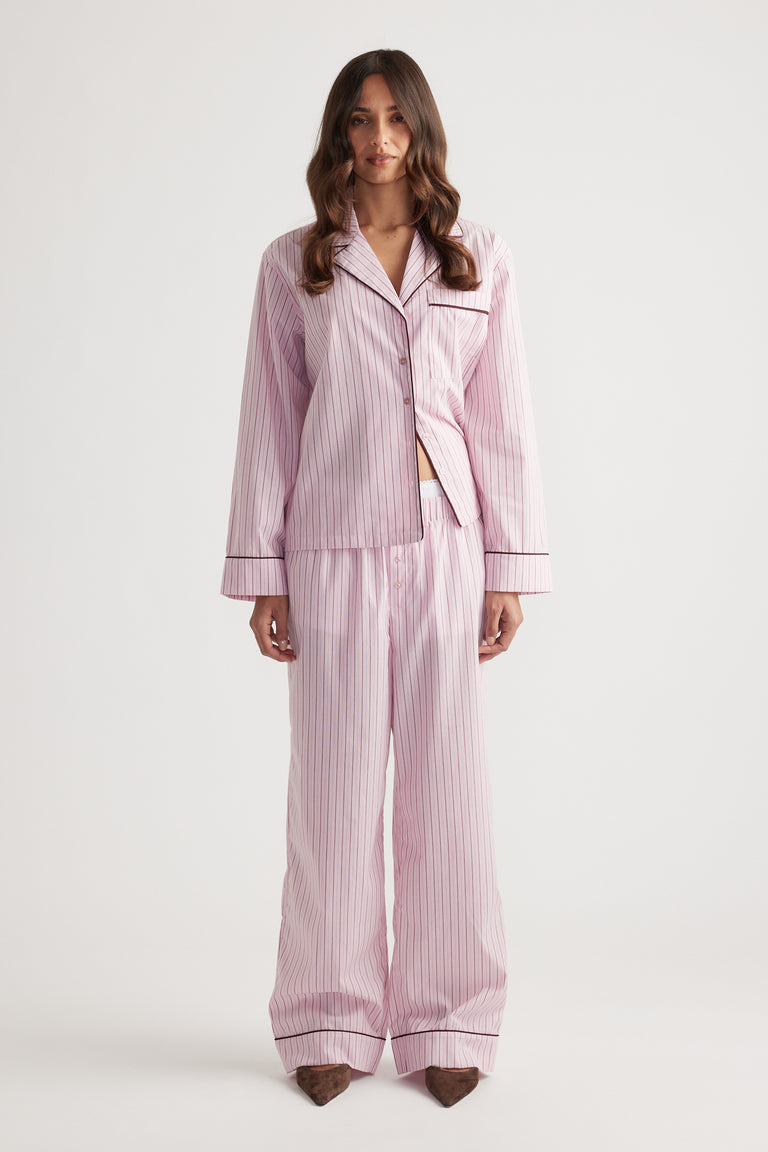 Woman wearing soft pink striped sleep wide leg pants and matching button-up long sleeve top with contrast piping trim