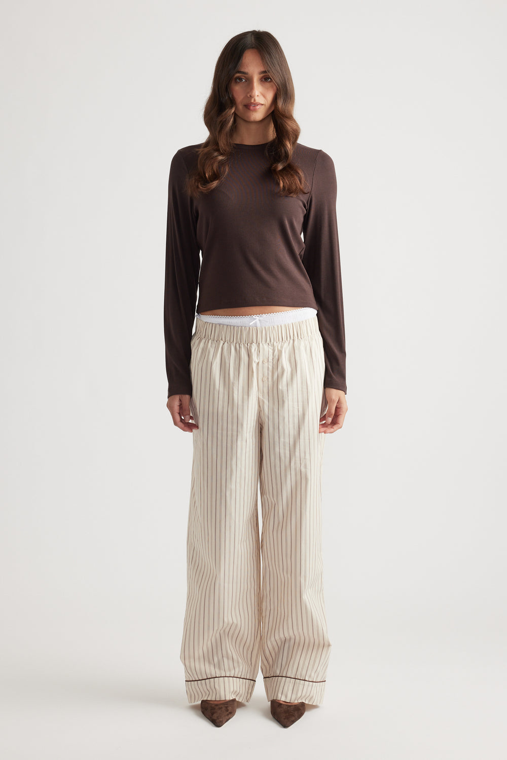 Woman wearing cream striped wide-leg pants with a gathered waistband paired with a fitted brown long-sleeve top