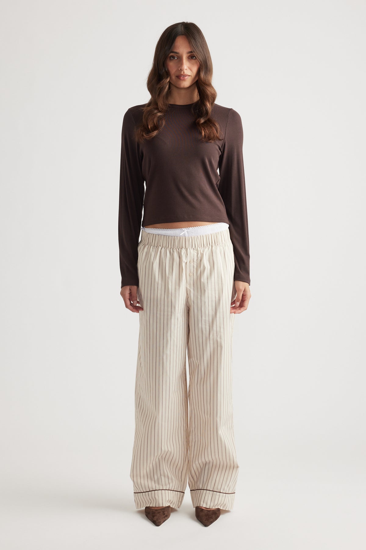 Woman wearing cream striped wide-leg pants with a gathered waistband paired with a fitted brown long-sleeve top
