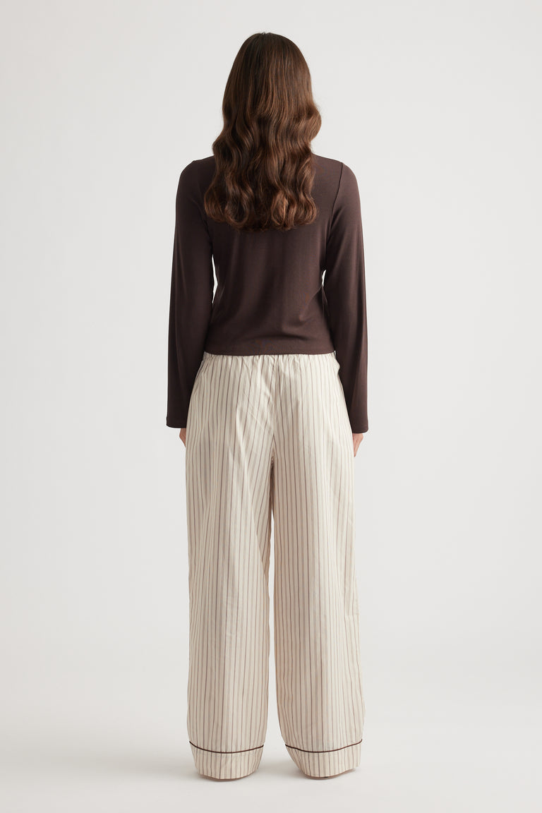 Woman wearing cream wide leg pants with thin vertical stripes and contrast piping at the hem for relaxed sleepwear style