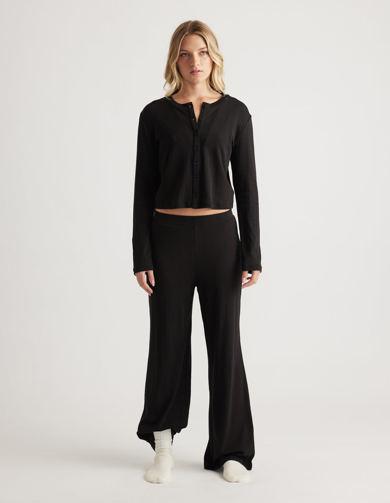 Woman wearing black sleep pointelle wide leg pants with a matching long sleeve button-up top in relaxed fit