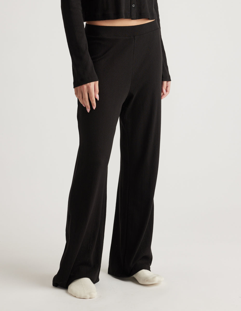 Woman wearing black wide-leg sleep pants with a subtle pointelle texture and an elastic waistband, paired with a black top