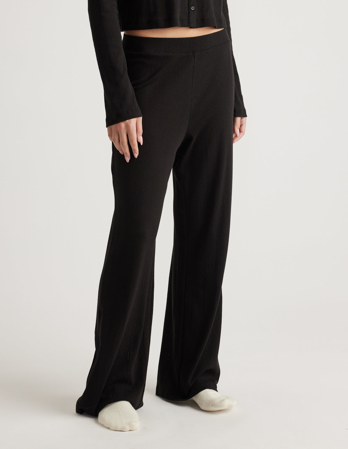 Woman wearing black wide-leg sleep pants with a subtle pointelle texture and an elastic waistband, paired with a black top