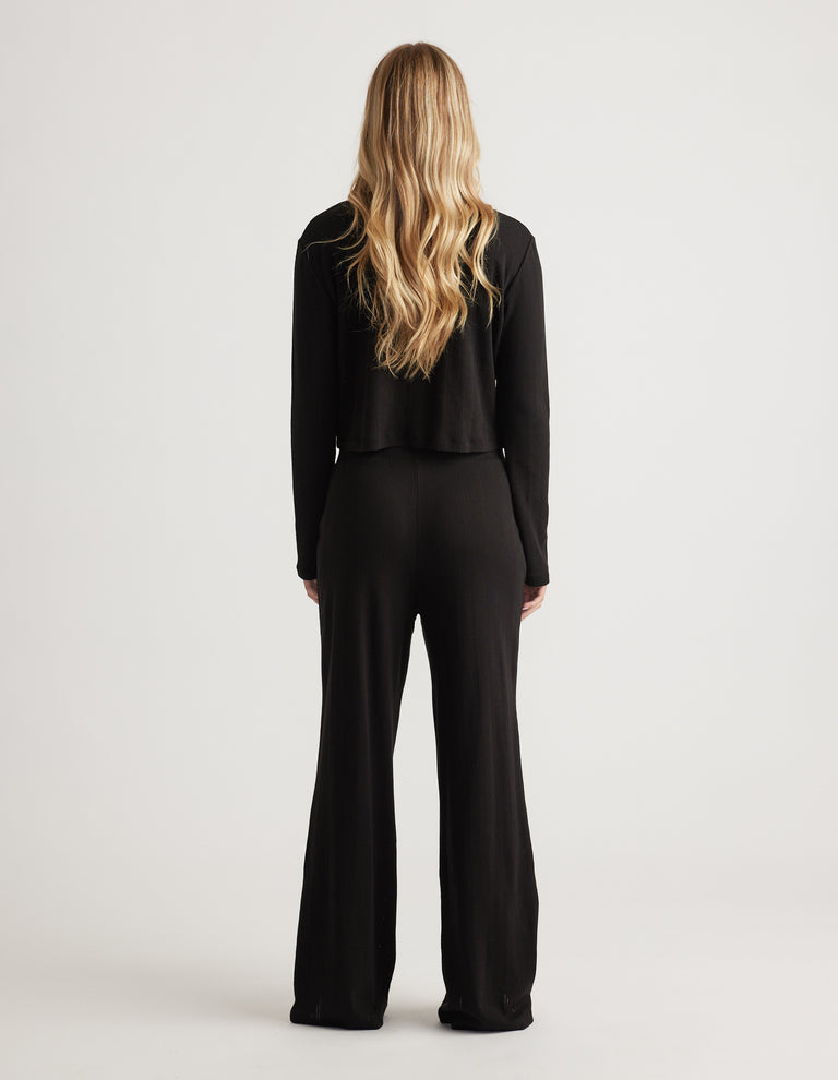 Back view of woman wearing black wide leg sleep pants in soft pointelle fabric with relaxed fit waistband